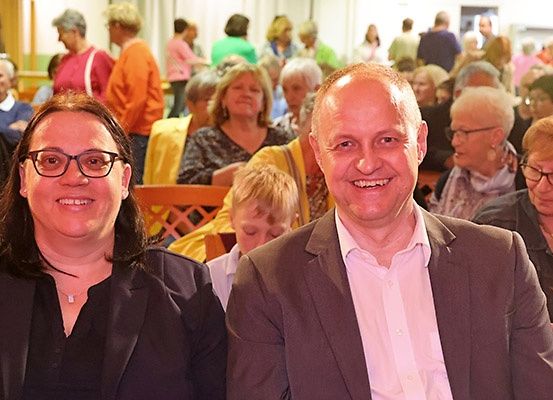 Zwei Personen, ein Mann und eine Frau, lächeln und posieren für ein Foto. Sie stehen mitten in einer Menschenmenge.