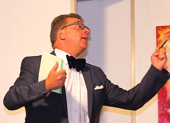 Ein Mann in formeller Kleidung hält einen Stift und Papier in der Hand und hält eine Rede bei einer Veranstaltung.