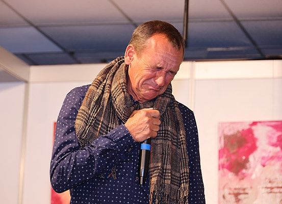 Ein Mann steht vor einem Mikrofon, hält einen Schal um den Hals und sieht nach unten.