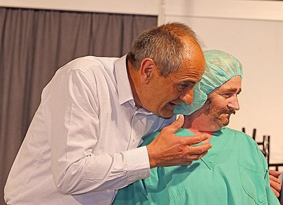 Ein Mann in einem weißen Hemd hält eine Frau in grüner OP-Kleidung, möglicherweise in einem Krankenhaus.