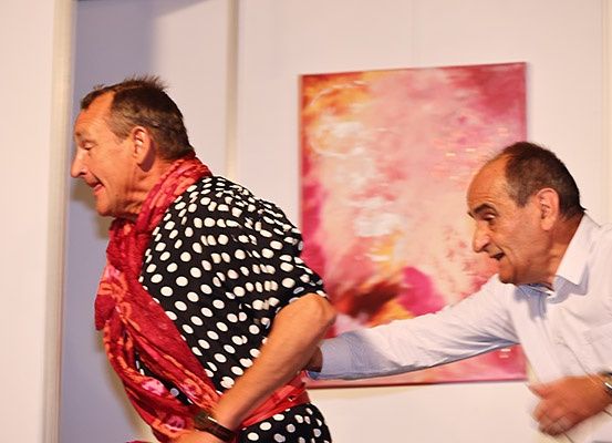 Zwei Männer lachen und haben einen spielerischen Moment in einem Raum mit einem farbenfrohen Gemälde an der Wand.