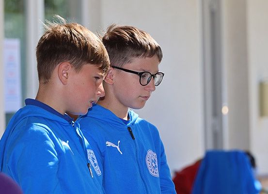 Zwei Jungen in blauen Hoodies mit weißen Logos stehen zusammen und warten möglicherweise oder schauen sich etwas an.