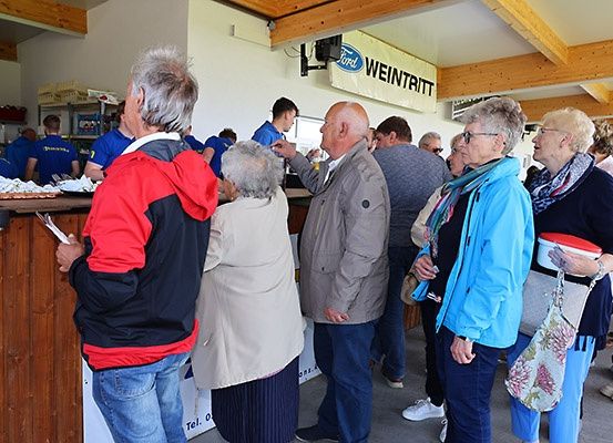 Eine Gruppe von Menschen steht in einer Schlange an einem Essenstresen, mit einem Banner über ihnen, das Ford Weintritt liest.