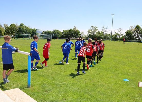 Fußballspieler in blauen und roten Trikots auf einem Feld, wobei ein Spieler in Blau einen Ball hält.