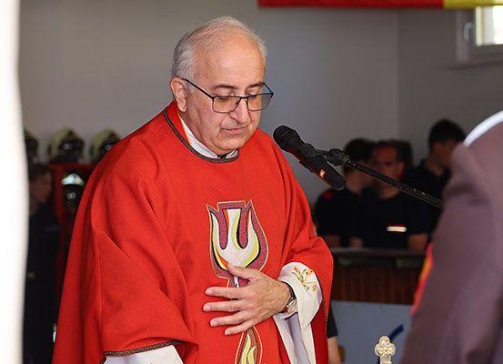 Ein Priester in einem roten Gewand spricht vor einem Publikum in ein Mikrofon.