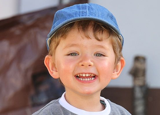 Ein junger Junge mit blauer Mütze und grauem Shirt lächelt mit einigen fehlenden Zähnen.