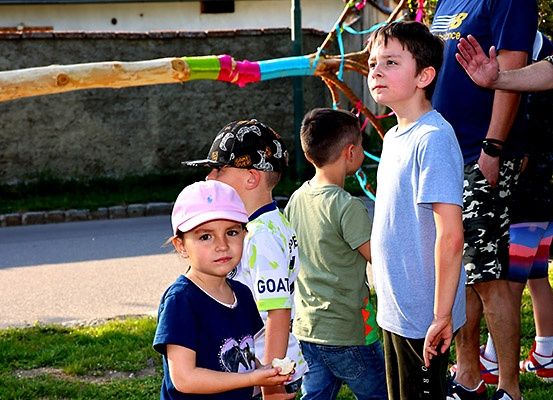 Mehrere Kinder stehen vor einem dekorierten Baumzweig, einige schauen nach oben, während ein Kind etwas in der Hand hält.