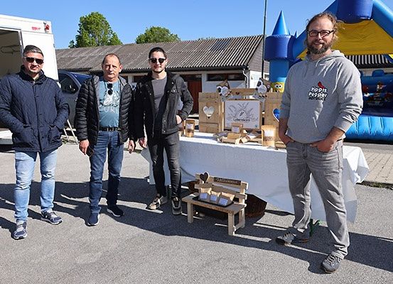 Vier Männer stehen vor einem Tisch mit Produkten, ein LKW ist hinter ihnen geparkt und ein aufblasbarer Burg im Hintergrund.