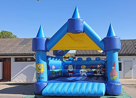Ein blauer und gelber aufblasbarer Sprungburg mit Cartoon-Charakteren steht draußen in der Sonne.