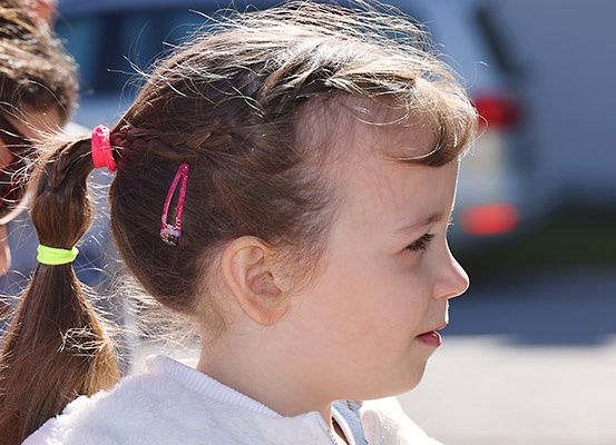 Ein kleines Mädchen mit braunen Haaren hat seine Haare mit pinken und grünen Haarklammern zu Zöpfen gebunden. Sie schaut nach unten.