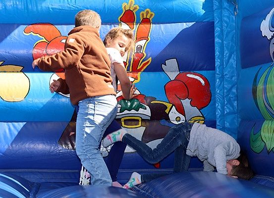 Drei Kinder spielen in einem blauen aufblasbaren Hüpfburg mit gezeichneten Cartoon-Charakteren an den Wänden.