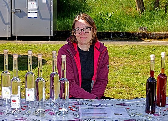 Eine Frau mit Brille lächelt, während sie vor einem Tisch mit mehreren Flaschen Schnaps sitzt.