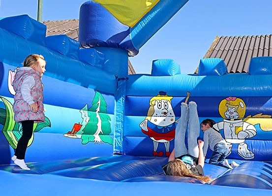 Zwei Kinder spielen in einem blauen aufblasbaren Sprungburg mit Zeichentrickfiguren an der Seite.