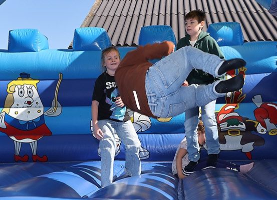 Drei Kinder spielen in einem blauen aufblasbaren Schloss mit Comicfiguren. Ein Kind führt einen Handstand durch.