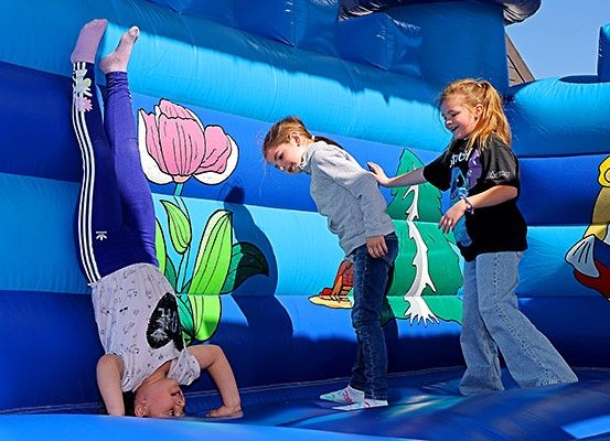 Drei junge Mädchen spielen in einem blauen aufblasbaren Sprunghaus. Ein Mädchen ist auf dem Kopf stehend, während die anderen zusehen.