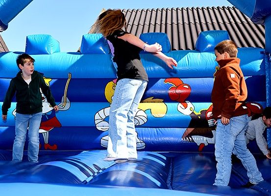 Vier Kinder spielen auf einer blauen aufblasbaren Burg mit Comic-Charakteren. Ein Junge steht vorne, ein Mädchen balanciert, und zwei Jungen beobachten von den Seiten.
