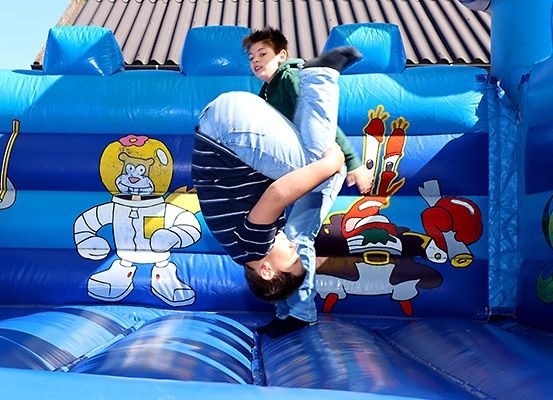 Zwei junge Jungen spielen in einem blauen aufblasbaren Sprunghaus, einer steht auf dem Rücken des anderen.