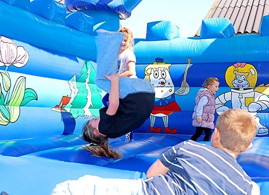 Mehrere Kinder spielen in einem blauen aufblasbaren Sprunghaus, wobei ein Mädchen einen Handstand macht und ein Junge auf dem Boden liegt.