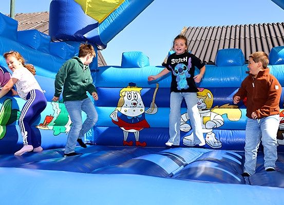 Vier Kinder spielen in einem blauen aufblasbaren Sprunghaus mit Zeichentrickfiguren unter klarem Himmel.