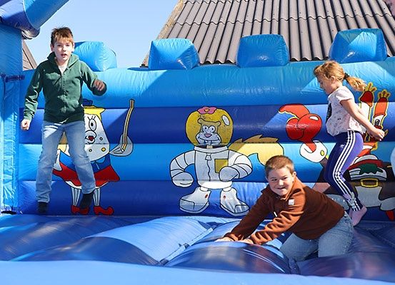 Vier Kinder spielen in einem großen blauen aufblasbaren Hüpfburg, die mit Zeichentrickfiguren verziert ist.