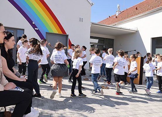 Eine Gruppe von Kindern in weißen T-Shirts geht in einer Reihe vor einem Gebäude mit einem gemalten Regenbogen an der Wand.