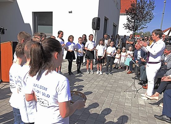 Eine Gruppe von Kindern in weißen T-Shirts tritt auf der Straße auf, während ein Mann klatscht und eine Menge zuschaut.