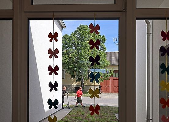 Zwei Kinder spielen draußen in der Nähe eines Hauses mit einer Schmetterlingsdekoration am Fenster.