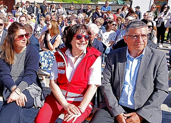 Eine Gruppe von Menschen in roten und weißen Westen sitzt zusammen im Freien, mit vielen anderen dahinter.