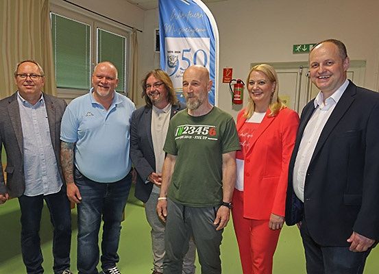 Eine Gruppe von Menschen in formeller und lässiger Kleidung steht zusammen in einem Raum mit einem Banner hinter ihnen.