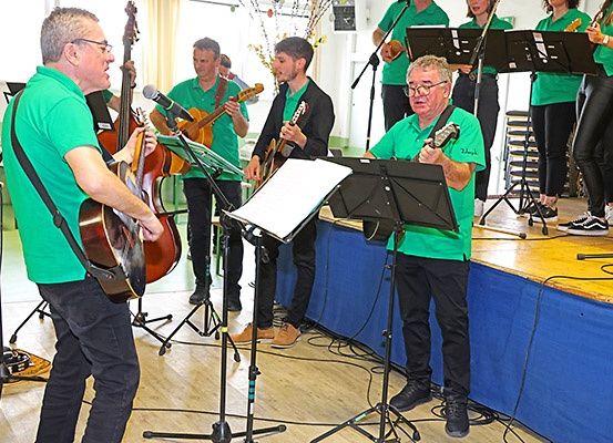 Eine Gruppe von Musikern in grünen Shirts und schwarzen Hosen spielt Gitarren auf einer Bühne mit Mikrofon und Notenständern.