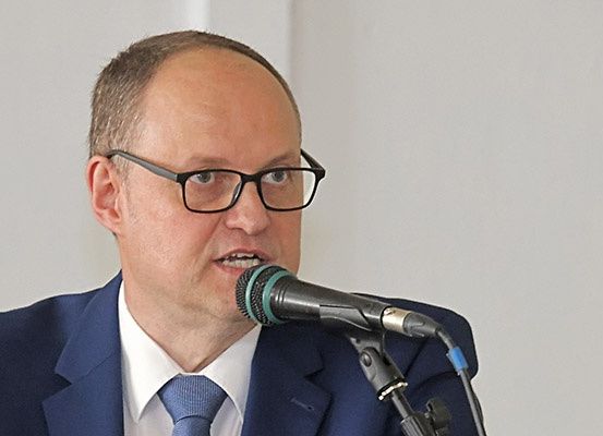 Ein Mann in einem blauen Anzug und Krawatte, der eine Brille trägt, spricht in ein Mikrofon.