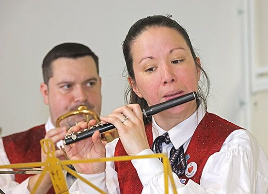 Eine Frau spielt Flöte und ein Mann Trompete, beide tragen rote Westen über weißen Langarmhemden und schwarzen Krawatten.