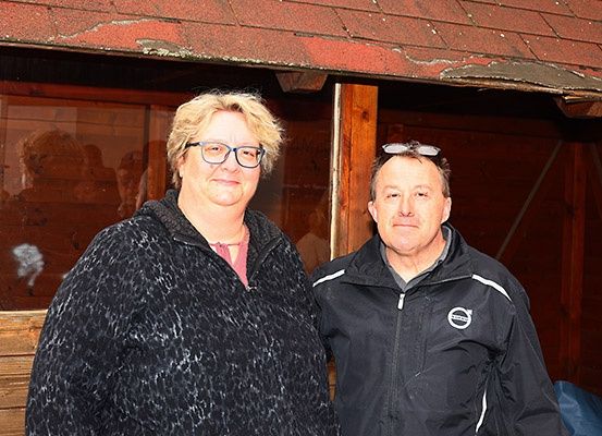 Ein Mann und eine Frau stehen zusammen vor einem Gebäude. Der Mann trägt eine Jacke mit Logo.