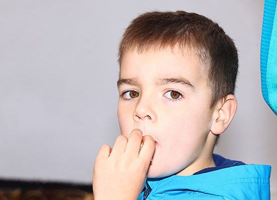 Ein junger Junge in einem blauen Jackett isst etwas mit seiner Hand in der Nähe seines Mundes.