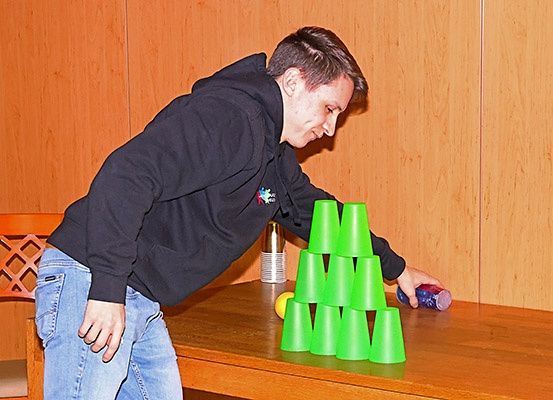 Ein junger Mann versucht, Becher auf einem Tisch zu stapeln und lächelt.