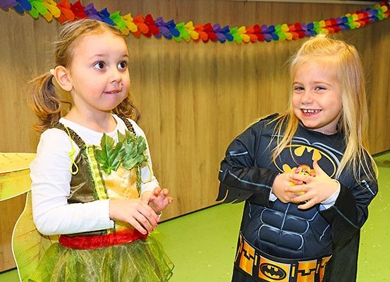 Zwei junge Mädchen in Kostümen, eines als Fee und das andere als Batman, lächeln und posieren für ein Foto.