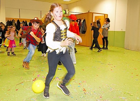 Eine Gruppe von Kindern in verschiedenen Kostümen spielt mit einem gelben Ball in einem grünen Raum.