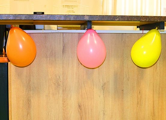 Drei Ballons in Orange, Pink und Gelb hängen von einem hölzernen Tresen ab.