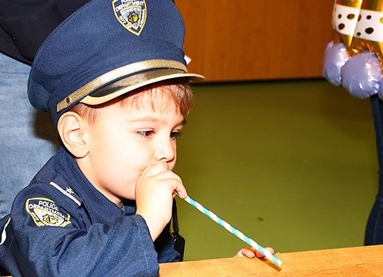 Ein kleiner Junge in einem Polizeiuniform bläst in einen blau-weiß gestreiften Strohhalm bei einer Veranstaltung.