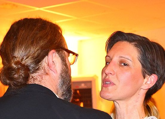 Ein Mann mit Bart und Brille schaut eine Frau mit kurzen Haaren an, die ihm zu sprechen scheint.