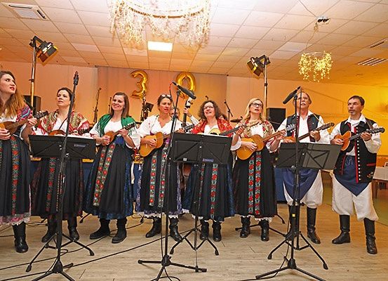 Eine Gruppe von Musikern in traditioneller Kleidung spielt auf der Bühne mit Gitarren, begleitet von einer Kristallleuchte und Luftballons im Hintergrund.