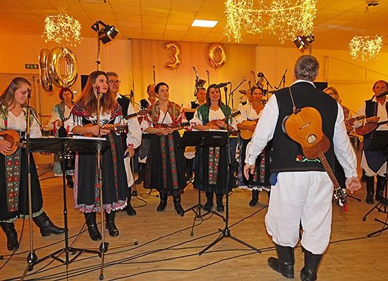 Eine Gruppe von Musikern, gekleidet in traditioneller Kleidung, spielt auf der Bühne mit Gitarren und anderen Instrumenten. Die Bühne ist mit Luftballons und Lichtern geschmückt.