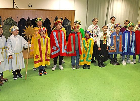 Eine Gruppe von Kindern in bunten Kostümen, möglicherweise für ein Theaterstück, stehen in einem Raum mit grünem Boden.