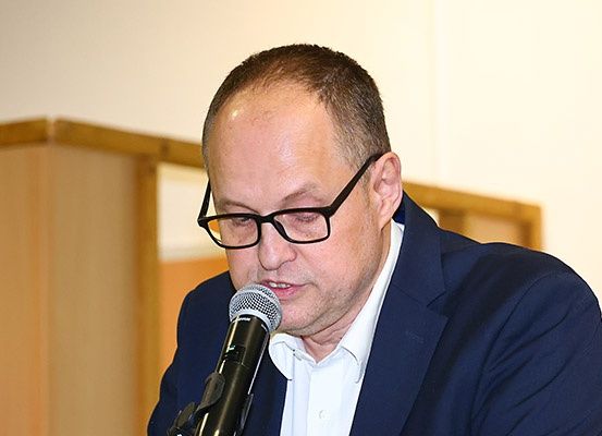 Ein Mann in Anzug und Brille spricht in ein Mikrofon, wahrscheinlich bei einer Konferenz oder Besprechung.