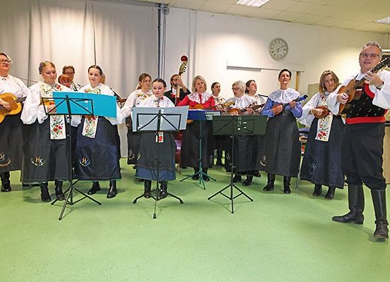 Eine Gruppe von Menschen in traditioneller Kleidung spielt Gitarren und singt in einem Raum mit grünem Boden.