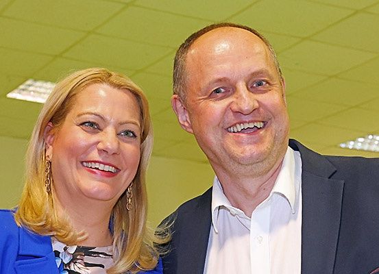 Ein Mann und eine Frau lächeln für ein Foto in einem Raum mit grüner Decke.