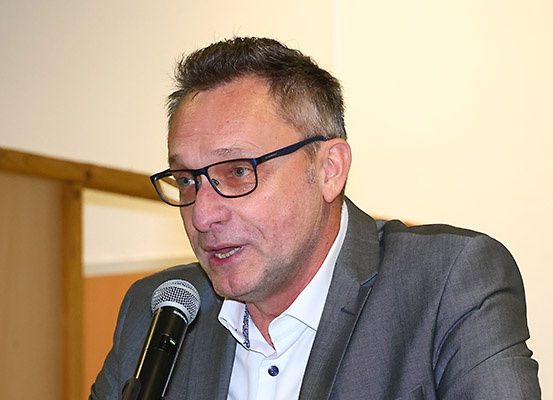 Ein Mann mit Brille spricht in ein Mikrofon auf einer Konferenz. Er trägt einen grauen Anzug und ein weißes Hemd.