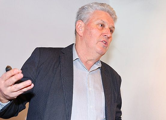 Ein älterer Mann in einem schwarzen Anzug und einem hellblauen Hemd spricht und gestikuliert mit seiner rechten Hand.