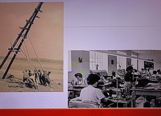 Ein geteiltes Bild zeigt zwei Szenen; links Arbeiter in Vintage-Uniformen ziehen einen umgefallenen Versorgungsmast; rechts arbeiten Frauen an Nähmaschinen in einer Fabrik.