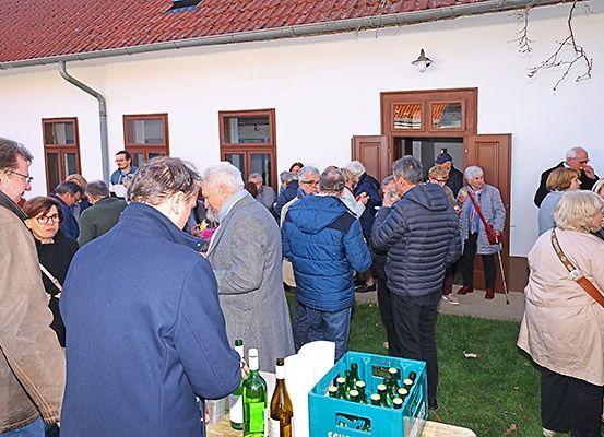 Eine Gruppe von Menschen in Winterkleidung versammelt sich um einen Tisch mit Weinflaschen und einer Kiste mit Flaschen vor einem Gebäude.
